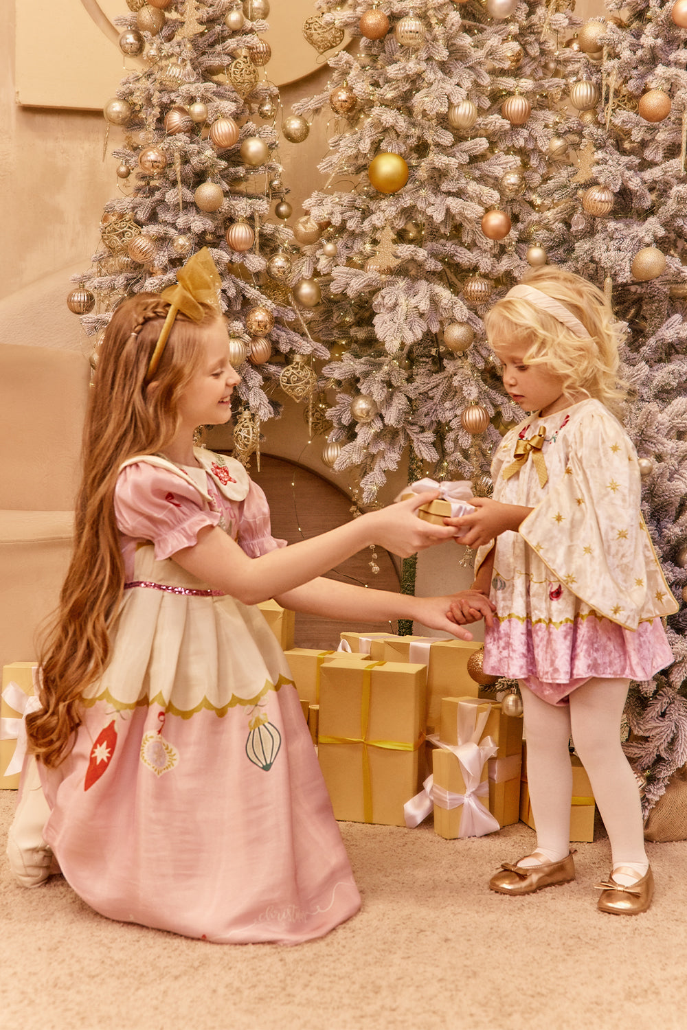Two young girls in dresses standing in front of a decorated Christmas tree.