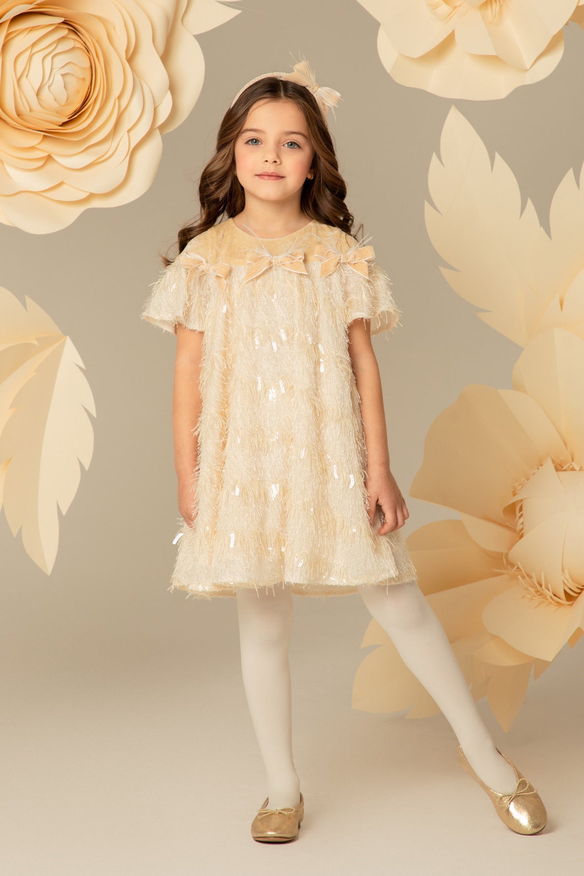 Girl wearing an ivory fringed dress with velvet bows