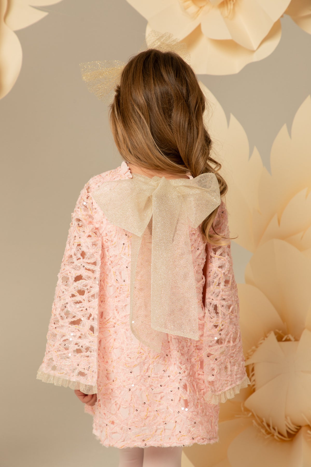 Back view showing the gold shimmering bow on a pink lace dress