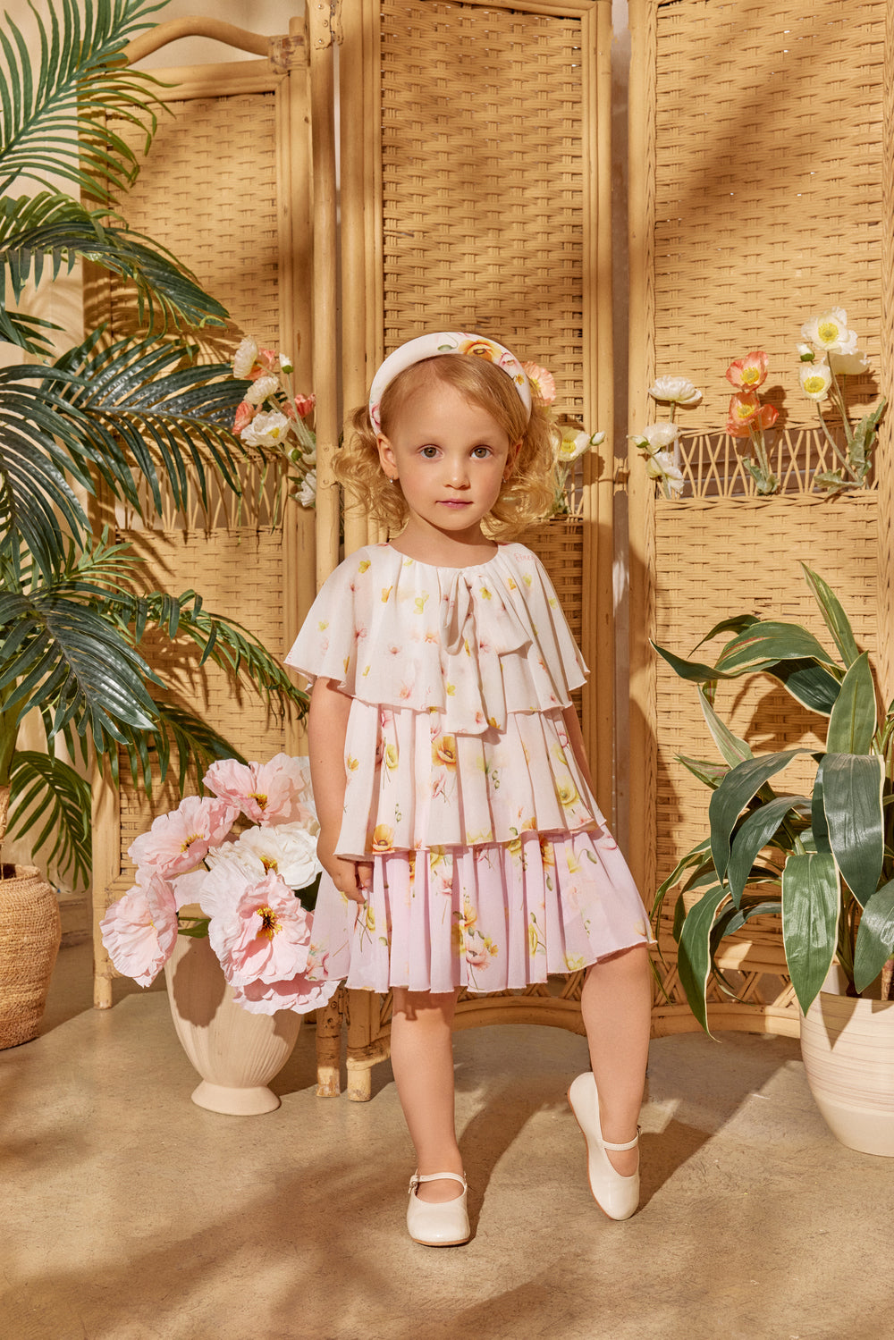 Young girl in a floral dress standing in a decorated room with plants and flowers.