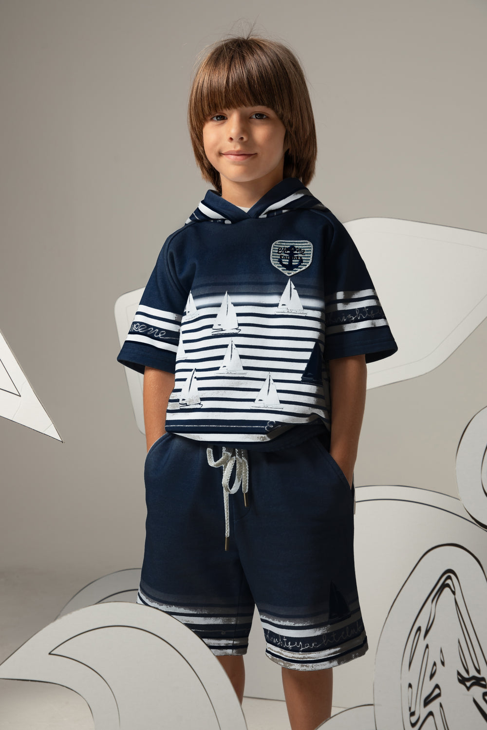 Child wearing a navy and white outfit with sailboat design, standing against a neutral background.