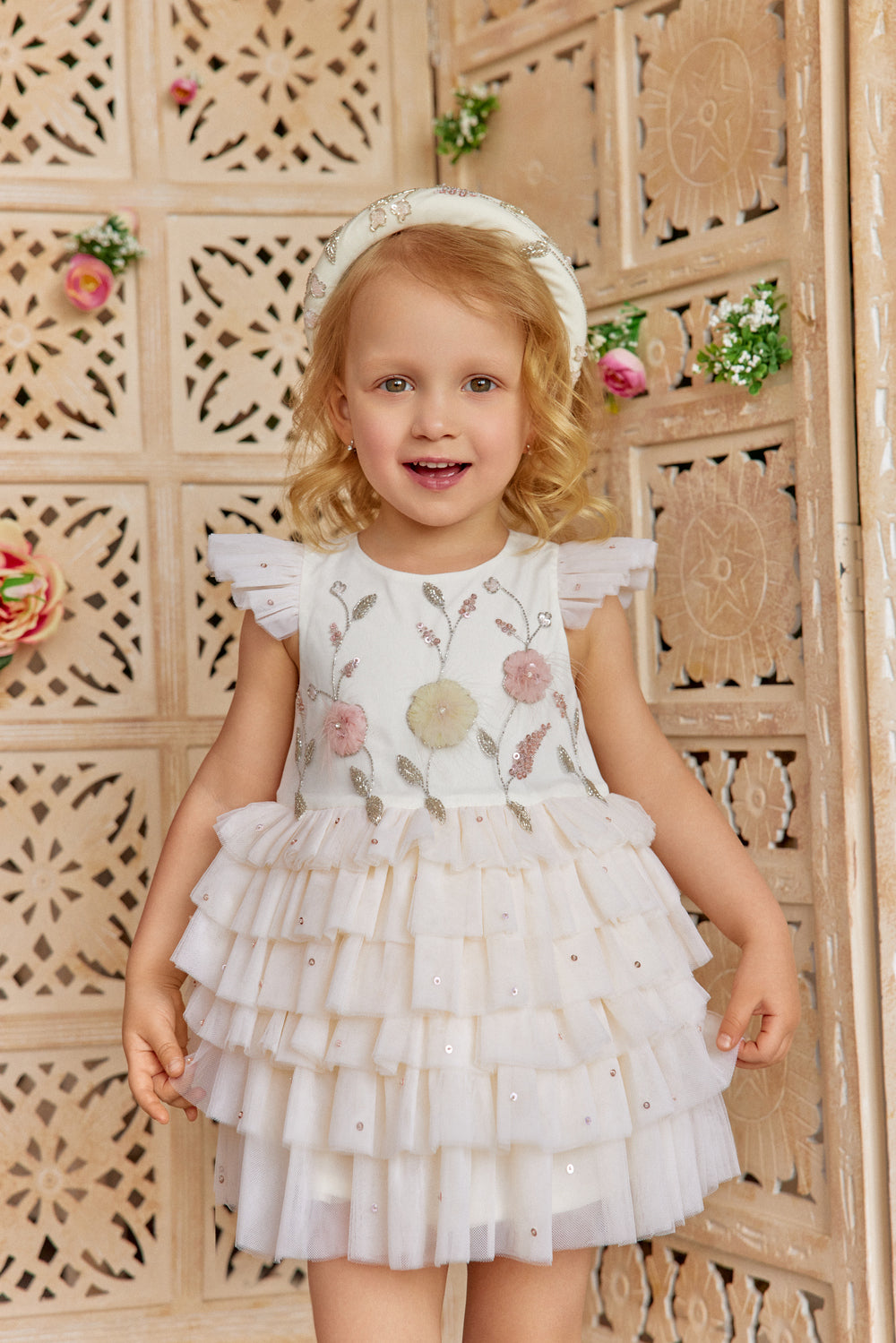 Young girl wearing a floral ivory dress with a decorative headband.
