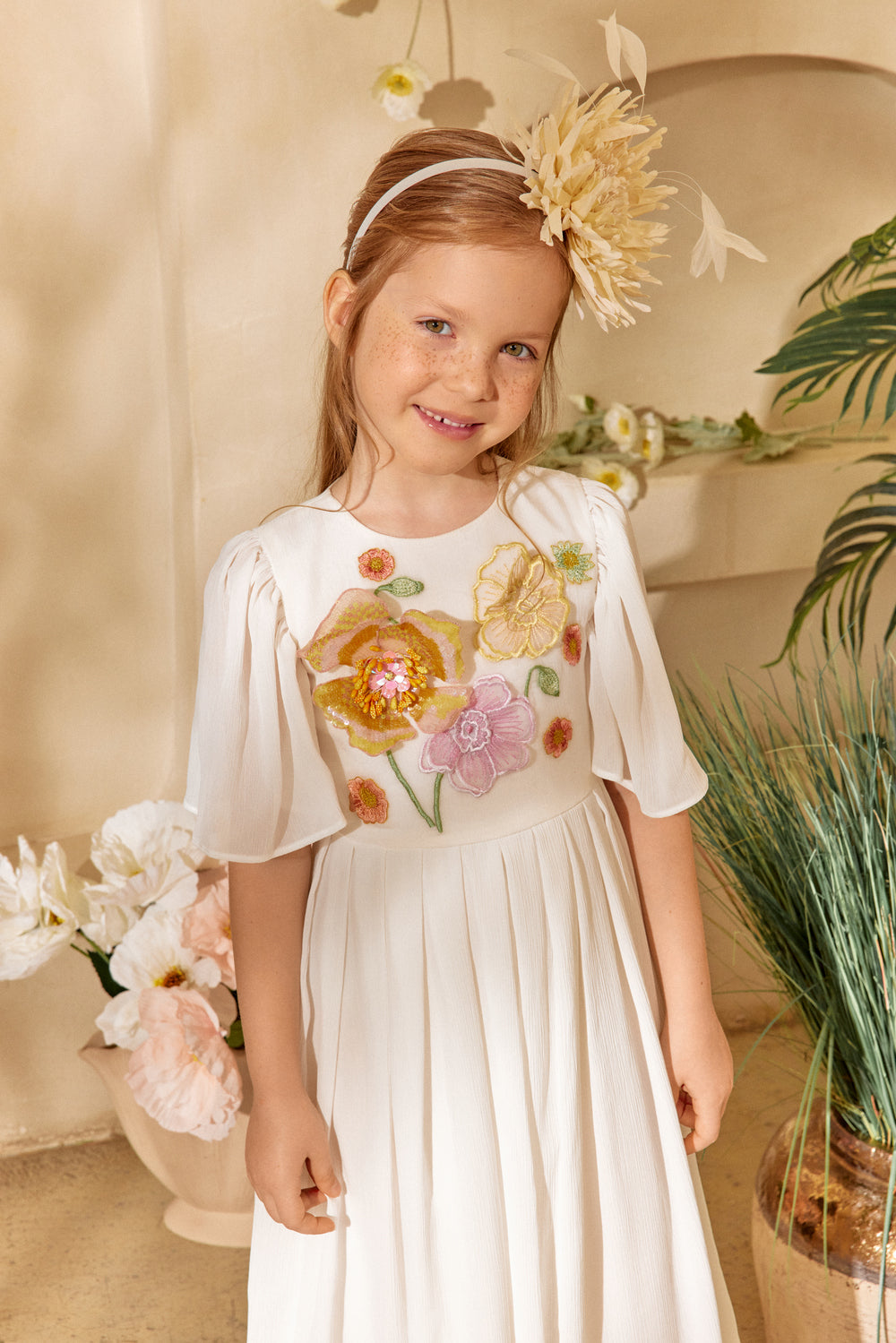 Young girl in a floral dress standing in a decorated room with flowers and plants.