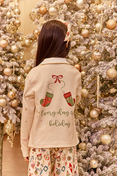 Girl wearing a Christmas-themed design pajama in front of a decorated Christmas tree.