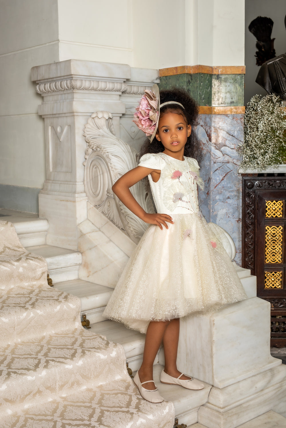 Young girl in a white dress sitting on marble steps with decorative elements.