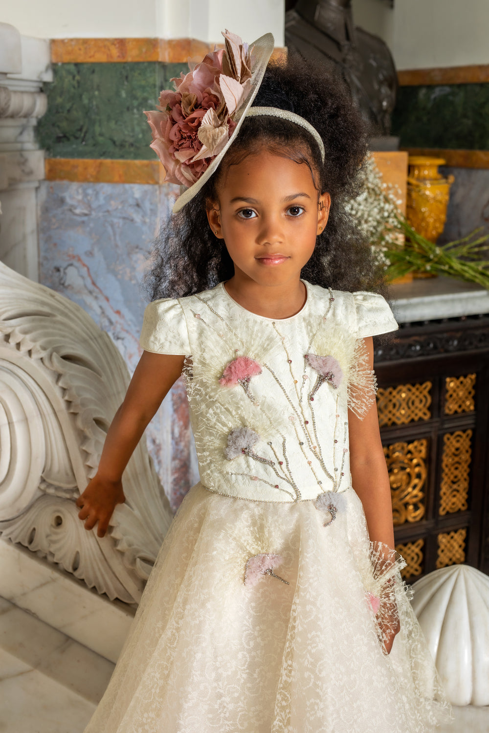 Young girl in a floral dress and headband standing indoors with decorative background
