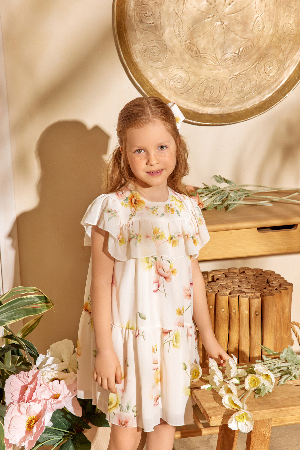 Young girl in a floral dress standing in a warm-toned room with decorative elements.