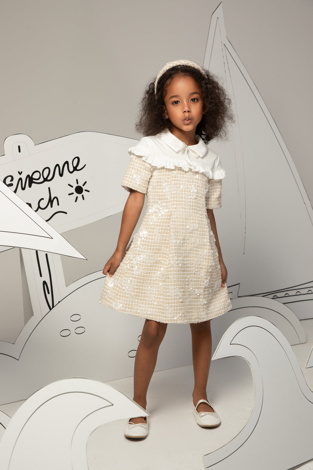 Young girl in a white dress standing in front of a stylized airplane cutout with 'Chicco' branding.