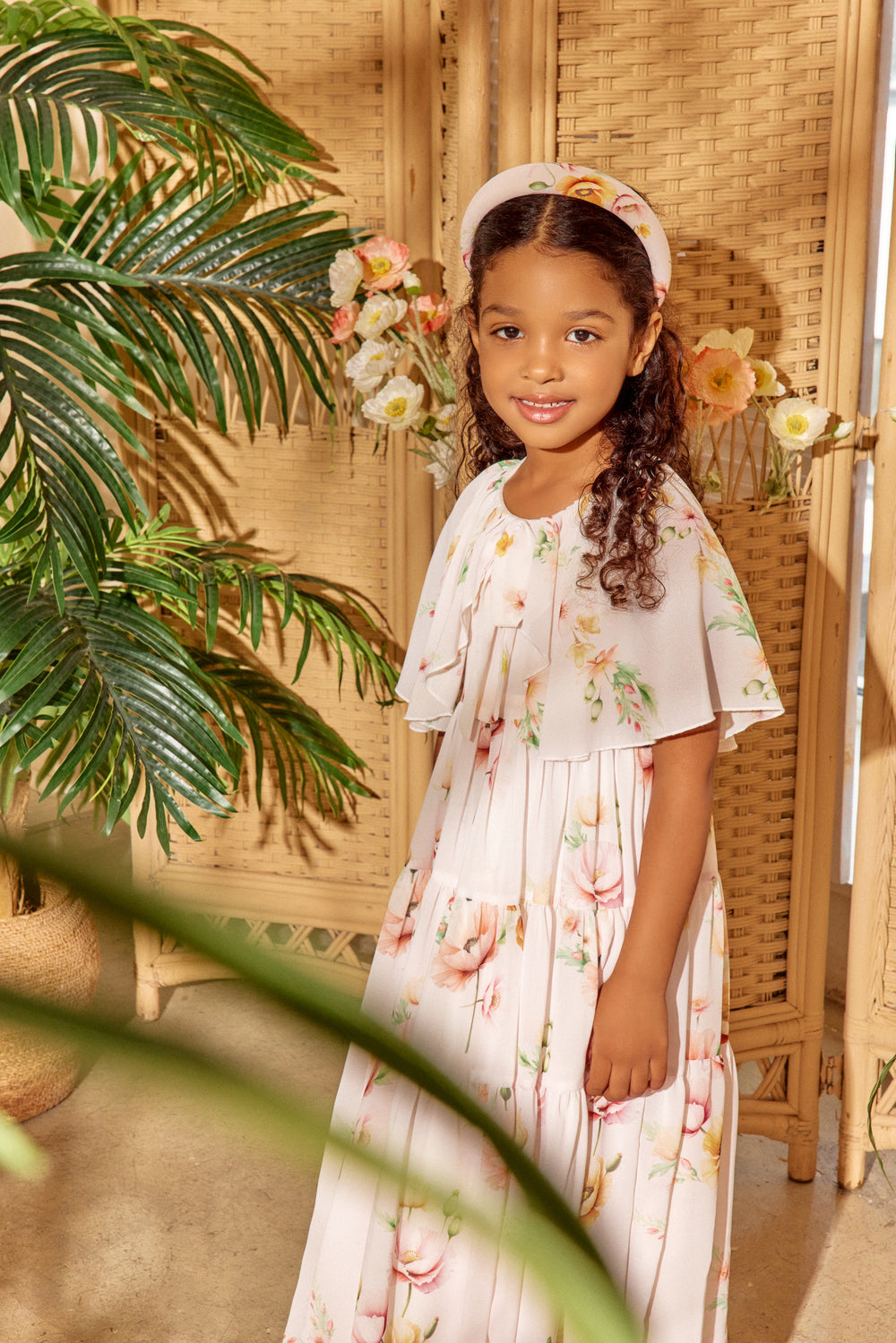 Young girl in a floral dress standing among plants and flowers.