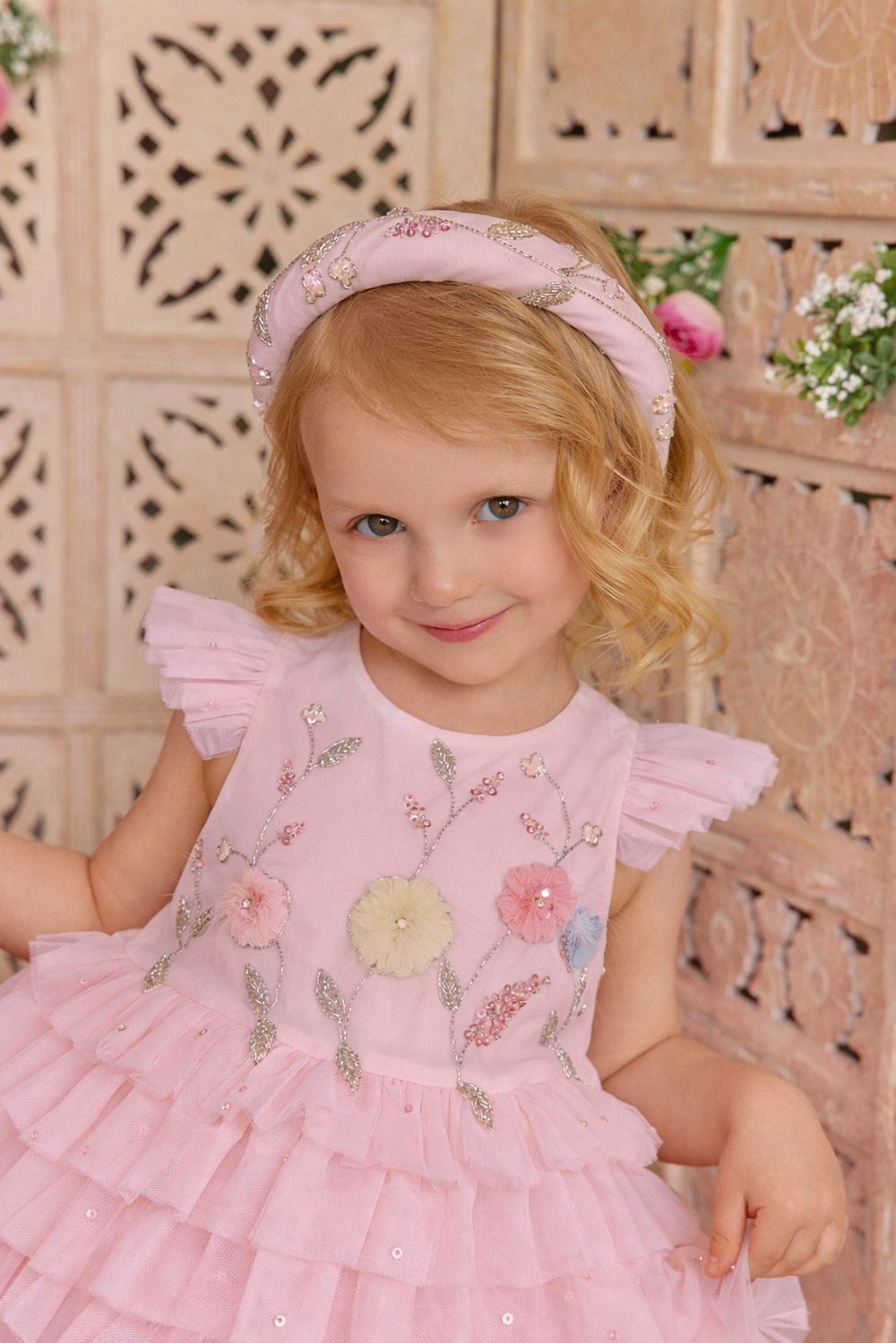 Young girl in a pink dress with floral embroidery and matching headband.