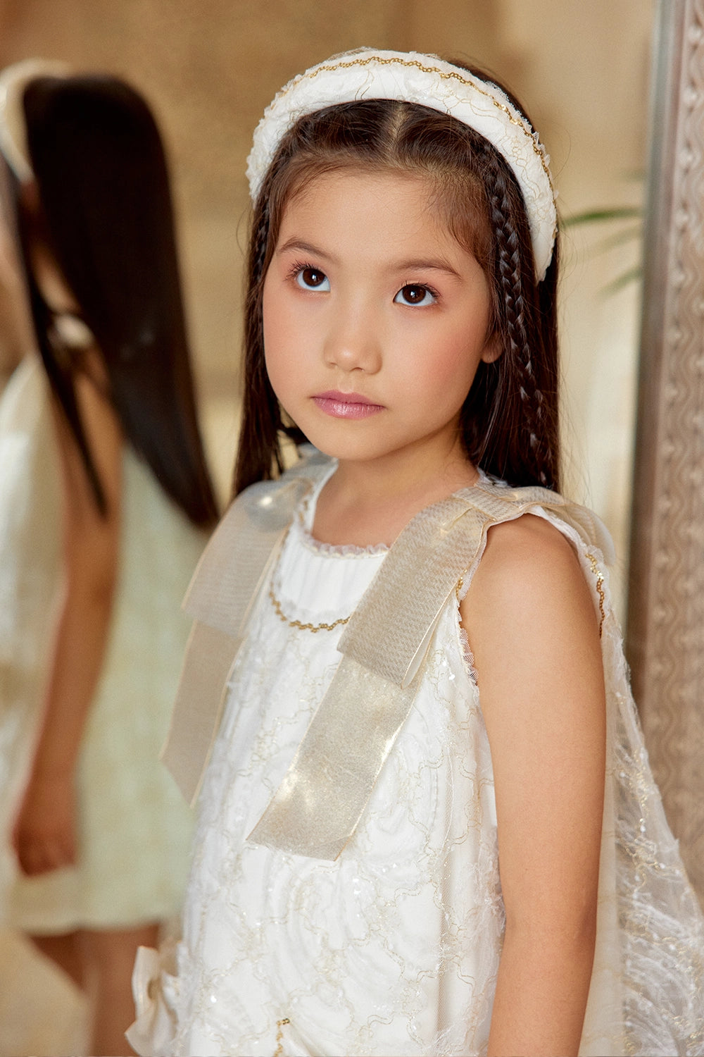 فستان دانتيل عاجي اللون بقصة حرف A مزين بفيونكات ذهبية على الكتفين وفيونكات على الجيوب