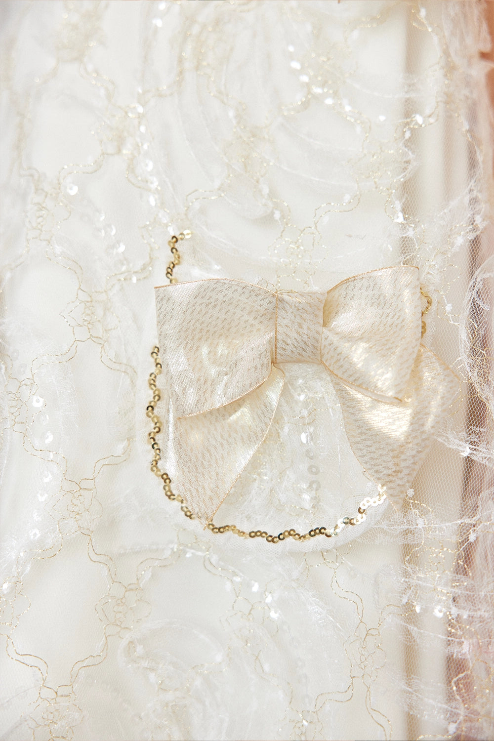 فستان دانتيل عاجي اللون بقصة حرف A مزين بفيونكات ذهبية على الكتفين وفيونكات على الجيوب