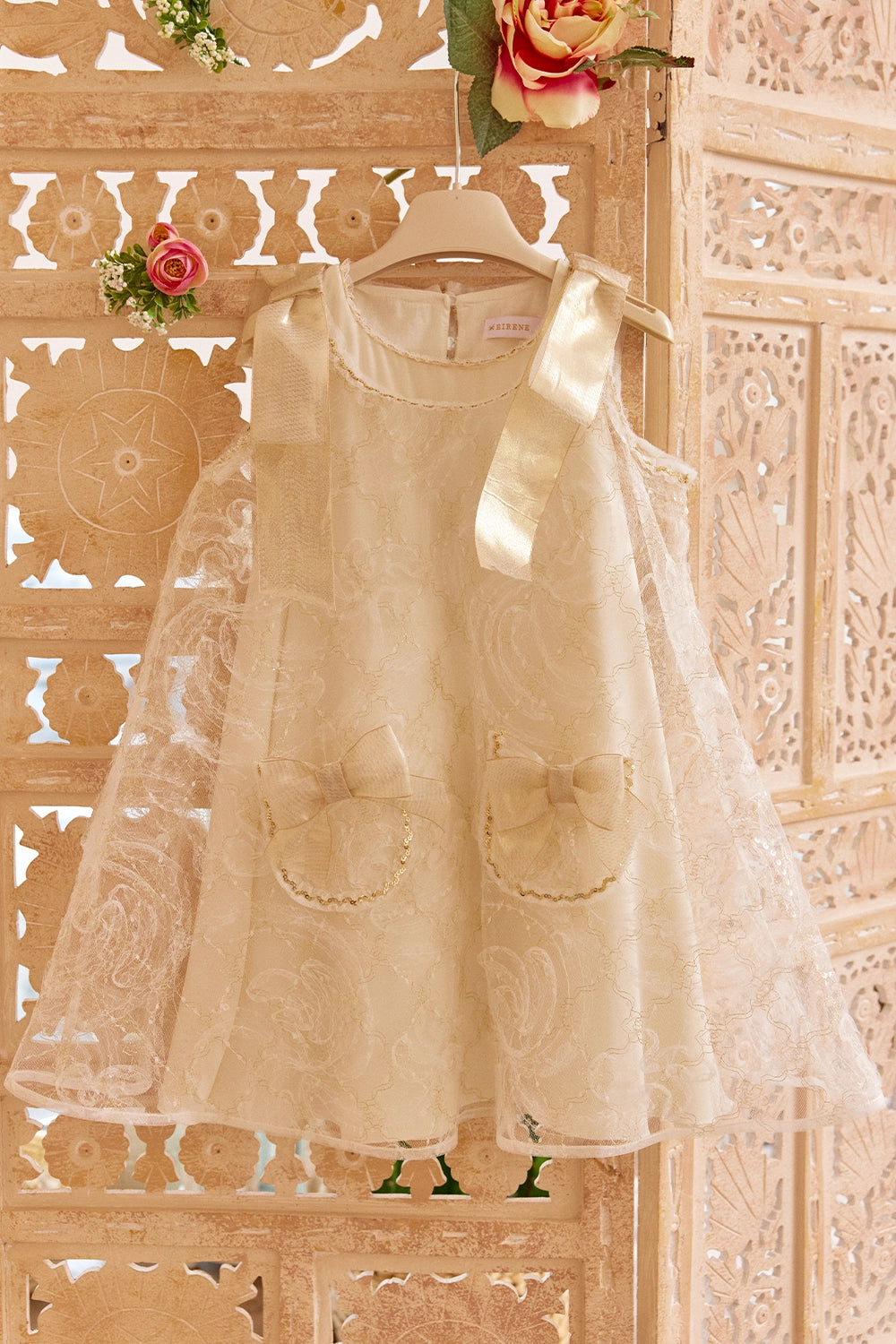 فستان دانتيل عاجي اللون بقصة حرف A مزين بفيونكات ذهبية على الكتفين وفيونكات على الجيوب