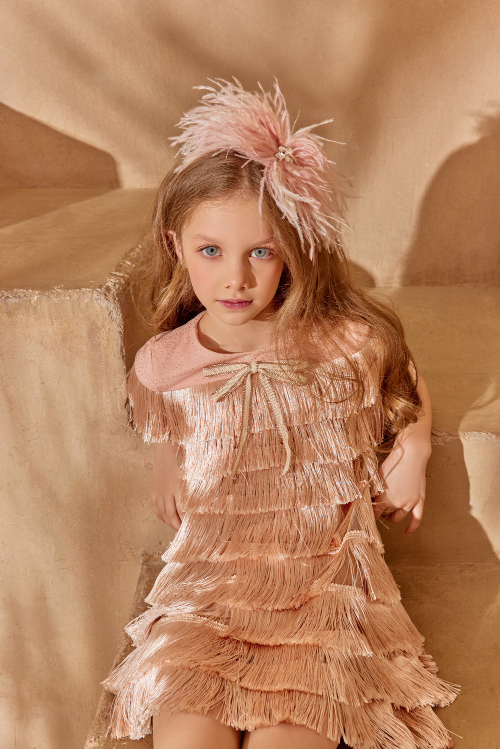 Young girl in a layered dress with a feather headband.