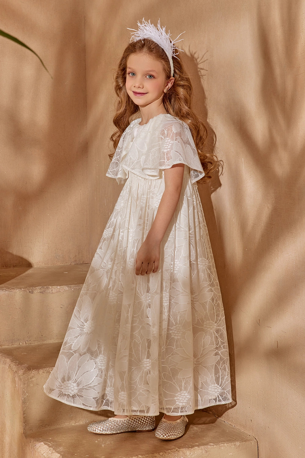 فستان من الدانتيل الزهري بلون أبيض كريمي بأكمام واسعة وعباءة، وفيونكة لامعة