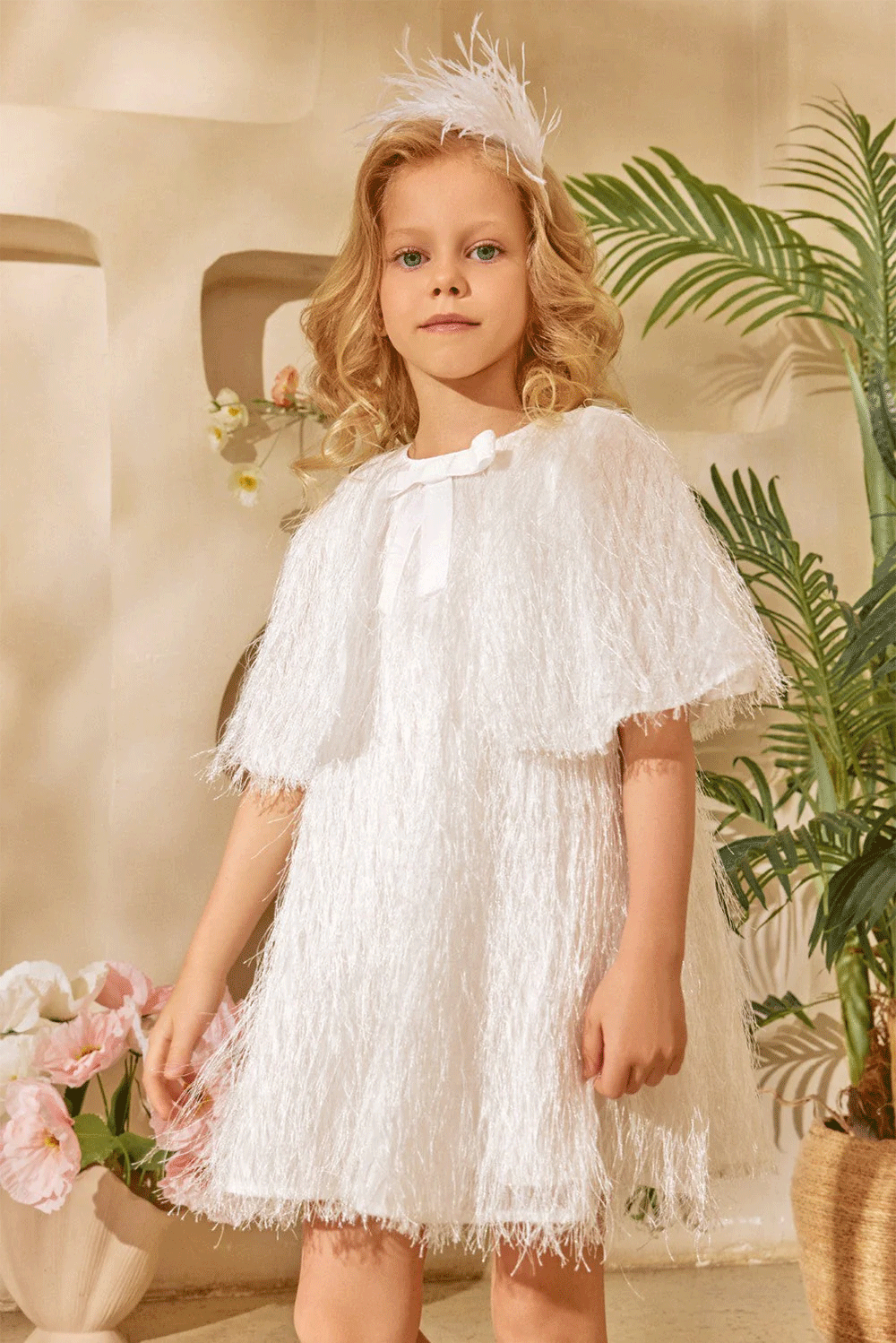 White dress with textured fringe shimmering fabric, featuring a cape-effect overlay and a bow detail