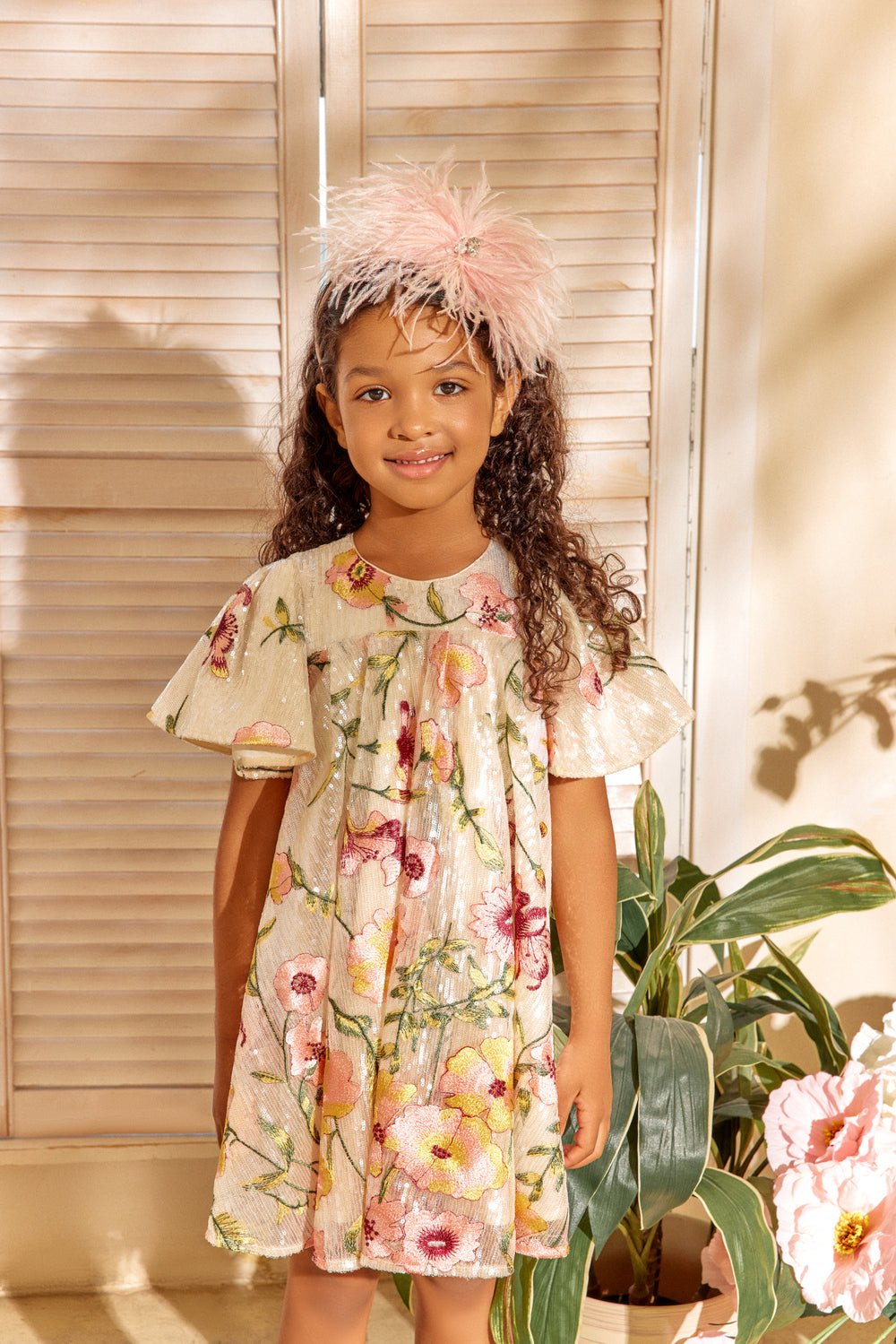 Girl smiling and posing dressed in a floral ivory sequin dress.