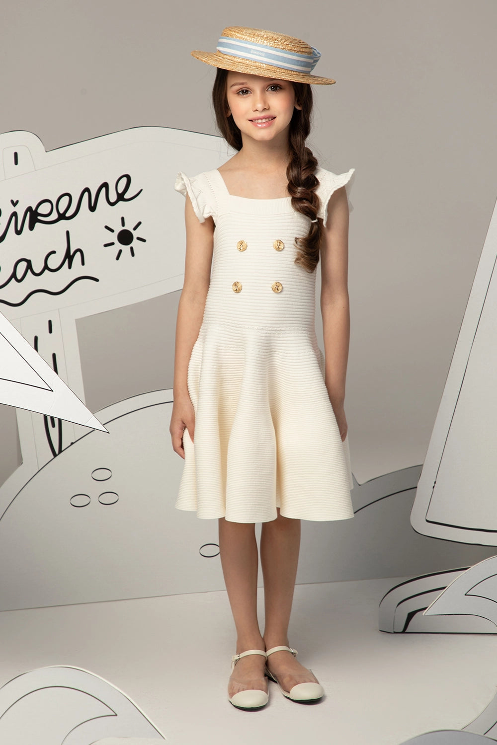 فستان محبوك بلون العاج ذو ملمس مميز، بتنورة واسعة، وأزرار ذهبية على شكل مرساة، وحمالات كتف مكشكشة.