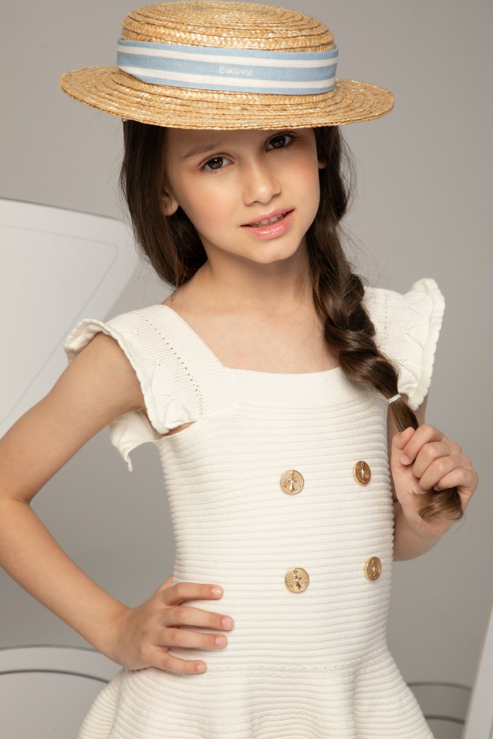 فستان محبوك بلون العاج ذو ملمس مميز، بتنورة واسعة، وأزرار ذهبية على شكل مرساة، وحمالات كتف مكشكشة.